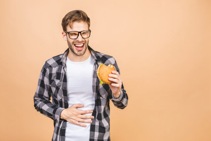 Young man holding a piece of hamburger. Student eats fast food. Your Stomach Acid Blocks Nutrition